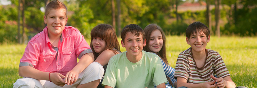 Teenager Jungen und Mädchen sitzen an einem sonnigen Sommertag auf der Wiese